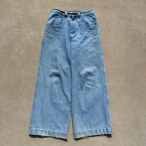 JNCO wide jeans ljusblå W31 L32 - Säljer ett par ikoniska JNCO jeans i ljusblå denim med extremt wide passform och råa, fransiga benslut. Klassisk femficksmodell med stora bakfickor och broderad JNCO-logga. Perfekta för dig som gillar streetwear och 90-talsvibbar.