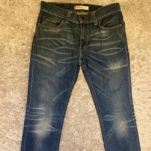 Levi's 511 Slim blå jeans W34 L32 - Snygga Levi's 511 Slim jeans i klassisk blå tvätt med coola slitningar och kontrastsömmar. Modellen har fem fickor, normal midja och raka ben med slim passform. Ikonisk läderpatch bak och röd Levi's-tag på fickan. Perfekta för en chill och stilren look.
