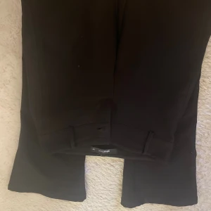 Svarta kostymbyxor från Gina Tricot XS - Svarta kostymbyxor från Gina Tricot i storlek XS. Byxorna har raka ben, bälteshällor och två bakfickor med lock och knapp. Snygg och stilren look som passar till många outfits. De är uppsydda så de passar perfekt för er som är runt 150cm