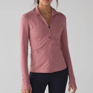Rosa träningsjacka från Lululemon - Säljer en snygg rosa träningsjacka från Lululemon med figurnära passform. Jackan har dragkedja framtill, höga fickor med dragkedja och tumhål vid ärmsluten. Perfekt för dig som vill ha en sportig look och bekvämt material. 
