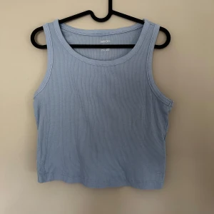 Ljusblå ribbad linnetopp från Esmara - Snygg ljusblå croppad linnetopp från Esmara. Toppen är ribbad och ärmlös med klassisk rund halsringning. Perfekt för varma dagar eller att styla lager på lager. Enkel och stilren design som passar till det mesta.
