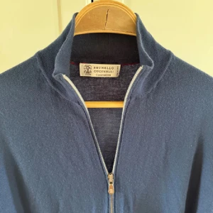  Brunello Cucinelli zip - Snygg blå kofta från Brunello Cucinelli i lyxig kashmir. Tröjan har hel dragkedja framtill, ribbade muddar och hög krage. Perfekt för dig som gillar stilrena och mjuka plagg med premiumkänsla.