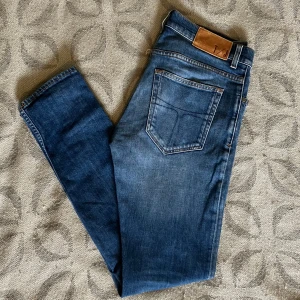 Tiger of Sweden jeans  - Snygga blå jeans från Tiger of Sweden med klassisk femficksdesign och diskreta slitningar framtill. Jeansen har raka ben, slim passform. Perfekta för en stilren  look.