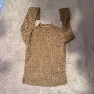 Beige stickad långärmad tröja - Snygg beige stickad tröja med lång ärm och diskret mönster i tyget. Tröjan har en högre halsringning och är perfekt för lager-på-lager. Den stickade strukturen ger en trendig och mysig känsla.