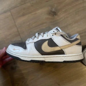 Nike Dunk Low i svart och vitt - Nike Dunk Low sneakers i svart och vitt med beige swoosh. Klassisk siluett med perforerad tå, snörning och platt sula. Perfekt för dig som gillar streetwear och retro vibes.💗