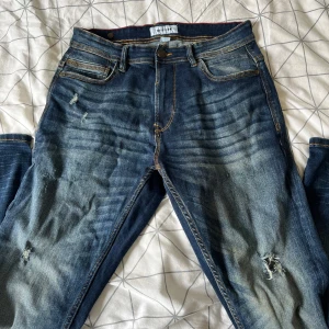 Levi's 511 blå jeans, storlek 31/32 - Säljer ett par Levi's 511 jeans i blå tvätt med slitningar och hål för en cool, avslappnad look. Klassisk femficksmodell med orange sömmar och läderpatch bak. Jeansen har en smal passform och är tillverkade i jeansmaterial.