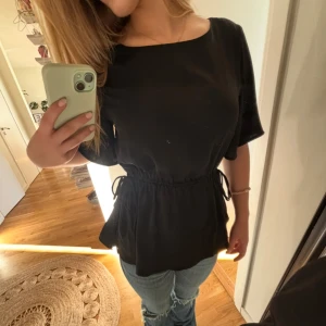Svart blus med knyt i midjan - Svart blus med lös passform och längre ärmar. Går att knyta på många olika sätt!! Toppen har rund halsringning och knytband i midjan som ger en snygg siluett. 