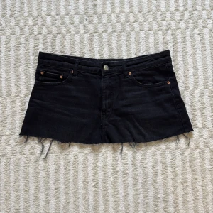 Svart jeanskjol från Gina Tricot - Svart kort jeanskjol från Gina Tricot i modellen Perfect Jeans. Det var från början ett par shorts som jag har klippt till en kjol.  Kjolen har rå, fransig kant nertill, klassiska jeansfickor fram och bak samt knapp och dragkedja framtill. Perfekt för en cool och avslappnad look.