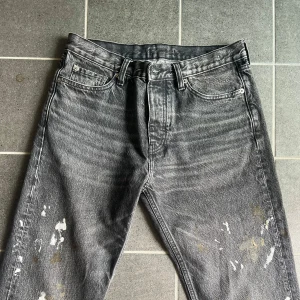 Hope Rush Denim splash jeans - Säljer ett par svarta HOPE Rush jeans i rak modell med coola färgstänk och slitningar. Jeansen har klassisk femficksdesign, bälteshällor och är tillverkade i bomull. Perfekta för dig som gillar en edgy och avslappnad stil. 