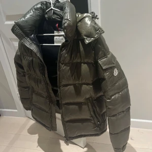 Moncler maya - Säljer nu min fina olivgröna Moncler Maya. Unik färg, perfekt för kalla dagar och riktigt snygg.🥹💞tagit väl handom den, finns inga repor eller skador! Storlek 2! Kom med prisförslag och skriv endast om du tänker köpa eller har fler frågor angående äktenhetsbevis osv. 