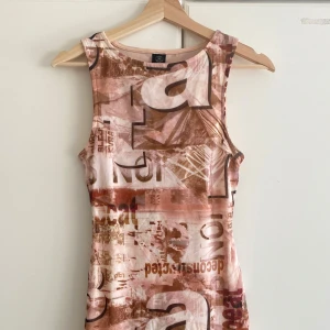 Beige och brun ärmlös kortklänning - Säljer en cool ärmlös kortklänning med tryckt grafiskt mönster i beige och bruna toner. Klänningen har en slim passform och är tillverkad i mjukt syntetmaterial som sitter skönt mot kroppen. Perfekt för dig som gillar unika prints och streetstyle.