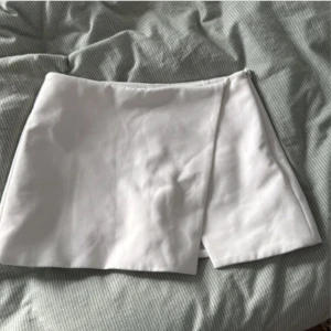 Vit omlottkjol från Zara - Säljer en stilren vit kortkjol från Zara med omlottdesign och dragkedja i sidan. Kjolen har en enkel och fräsch look som är lätt att matcha med olika toppar. Perfekt för dig som gillar minimalistisk stil.