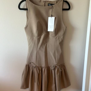 Beige klänning med rosetter  - Supersnygg beige kort klänning från Zara med markerad midja och volang nedtill med rosetter. Aldrig använd med lapp kvar 🫶🏼🫶🏼🤍🤍