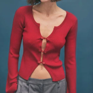 Röd ribbad kofta från NA-KD - Trendig röd ribbad kofta från NA-KD med croppad passform och snygga rosettdetaljer som knäppning framtill. Långärmad modell med lätt utsvängda ärmar och djup rundad ringning. Perfekt för dig som vill sticka ut med en cool och feminin look.