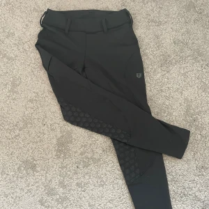 Svarta ridbyxor Maya Delorez XS - Säljer ett par svarta tjocka ridbyxor från Maya Delorez i storlek XS. De har mid waste midja, bälteshällor, snygga bakfickor med knapp och silikonprint på insidan av benen för extra grepp. Stretchigt och bekvämt material som passar perfekt till ridning.