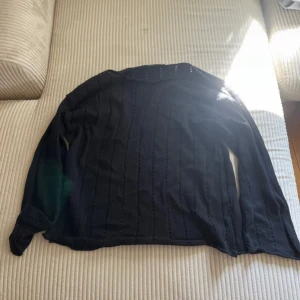 Svart stickad tröja från lager 157,strl M - Svart stickad tröja från 157 i storlek M. Tröjan har lång ärm och ett snyggt hålmönster i vertikala rader som ger en cool och luftig känsla. Perfekt att styla med jeans eller kjol för en chill look.