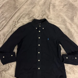 Mörkblå skjorta från Polo Ralph Lauren - Klassisk mörkblå skjorta från Polo Ralph Lauren. Bara använd ett par gånger då jag växt ur den. Storlek M (barnstorlek) Pris kan diskuteras!                    