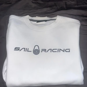 Vit Sail Racing sweatshirt i bomull - Vit sweatshirt från Sail Racing med broderad logga framtill. Klassisk rund halsringning och stilren design. Perfekt för dig som gillar sportig och clean stil. Tillverkad i mjuk bomull för skön känsla hela dagen.