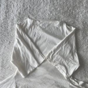 Vit omlottopp med knytband - Supersnygg vit omlottopp med trekvarts ärmar och breda knytband i midjan. Toppen är gjord i mjuk bomull som känns skön mot huden. Perfekt att styla med jeans eller kjol för en fräsch look.