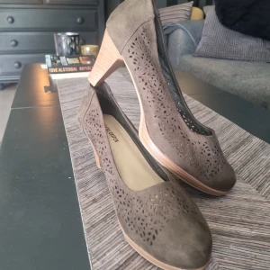 Gröna mockapumps med utskurna detaljer - Snygga gröna pumps från gyllene gripen i mocka med utskurna mönster på ovandelen. Skorna har rund tå och en stabil, låg klack i trälook. Perfekta för dig som vill ha en stilren och trendig sko med det lilla extra.