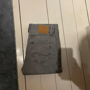 Grå relaxed jeans Jack & Jones 28/32 - Grå jeans från Jack & Jones i modellen Relaxed/Chris. De har en avslappnad passform med raka ben och klassisk femficksdesign. Jeansen är tillverkade i bomull och har en snygg, ljusgrå tvätt som passar till det mesta.