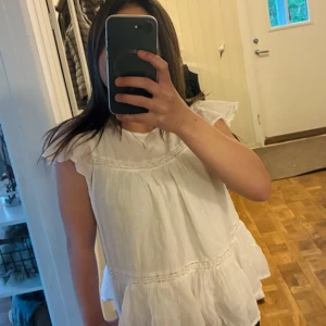 Vit volangblus från Gina Tricot - Supersöt vit blus från Gina Tricot med volangdetaljer och korta ärmar. Blusen har en luftig och flowy passform med fina spetsinslag och knäppning bak i nacken. Perfekt för en fräsch och somrig look!❤️🩷💕