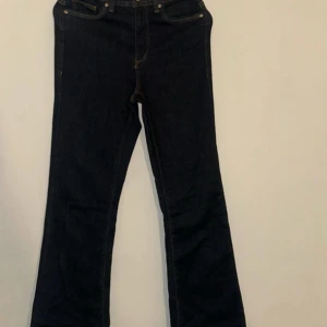 Bootcut jeans från ONLY i mörkblå denim - Snygga bootcut jeans från ONLY i mörkblå denim med klassiska gula sömmar. Modellen har fem fickor och en tidlös siluett som ger en schysst retrovibe. Perfekt för dig som gillar lite vidare ben och vill ha en cool look.