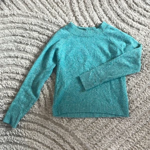 Turkos stickad tröja från Vero Moda - Mysig turkos stickad tröja från Vero Moda i storlek XS. Tröjan har rund halsringning, ribbade muddar och är långärmad. Perfekt för lager-på-lager och chill dagar. Enkel och stilren design som är lätt att matcha.