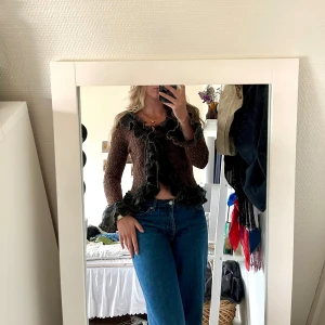 Vintage kofta med volang - Superfin brunmelerad kofta med svarta volangdetaljer längs kanterna och ärmsluten. Koftan är stickad och har en öppen front med knytband. Extremt cool kofta för dig som diggar vintage-stil, går att styla antingen som den är eller över ett annat plagg 