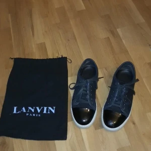 Svarta sneakers från Lanvin med lackad tå - Snygga svarta sneakers från Lanvin med vit sula och glansig, lackad tå. Skorna har klassisk snörning och en stilren design som passar till det mesta. Medföljer original dustbag från Lanvin Paris. Det finns en liten skade på vänstra tån men syns knappt vid användning 
