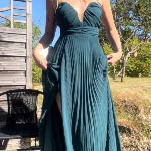 Petrolfärgad balklänning med slits - Superfin Petrolfärgad långklänning med djup v-ringning och tunna axelband. Köptes för en bal men kom aldrig till användning så säljs därför i nyskick med lappar kvar. Klänningen har plisserad kjol, markerad midja och en snygg slits på sidan. Toppen är rynkad med mesh-detalj i urringningen. Perfekt för bal eller fest! Skicka DM vid frågor. Nypris 750:-