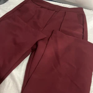 Vinröda kostymbyxor från SHEIN - Snygga vinröda kostymbyxor från SHEIN i storlek S. Byxorna har en klassisk rak passform med hög midja och är perfekta för en stilren look. Tillverkade i ett mjukt och lätt syntetmaterial som känns bekvämt hela dagen.