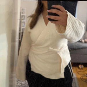 Vit omlott kofta i ribbstickad bomull - Superfin vit omlott kofta i ribbstickad bomull med knytband i midjan. Långa ärmar och mjuk känsla, perfekt för lager-på-lager. Snygg och enkel att styla till både jeans och kjol. För dig med storlek M&L