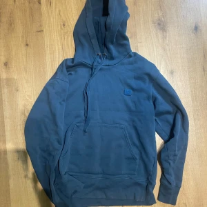 Blå hoodie från Acne Studios XS - Säljer en stilren marinblå hoodie från Acne Studios i storlek XS. Tröjan har huva med snörning, stor magficka och diskret Acne Studios-logga på bröstet. Tillverkad i mjuk 100% bomull, perfekt för chill dagar och streetwear-vibe.