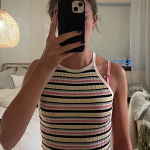 Randig ribbad linnetopp från H&M Divided - Säljer en ribbad linnetopp från H&M Divided i storlek S. Toppen har smala axelband och ett färgglatt randigt mönster i vitt, svart, rosa, gul och ljusblå. Materialet är mjukt och stretchigt med en slim passform, perfekt för en chill och färgstark look.