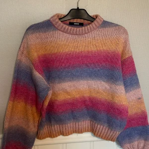 Randig stickad tröja  - Supermysig stickad tröja från BikBok i storlek S. Tröjan har breda ränder i rosa, blått, gult och beige, med en relaxed fit och ribbade muddar. Perfekt för dig som gillar färg och vill ha en chill vibe på hösten eller vintern.