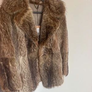 Brun pälsjacka med bred krage - Säljer en snygg brun pälsjacka med bred krage och klassisk passform. Jackan har naturliga färgskiftningar i brunt och beige, vilket ger en lyxig och trendig look. Perfekt för dig som vill sticka ut och hålla dig varm under kyliga dagar.