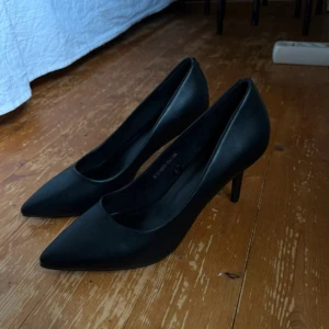 Svarta pumps med klack - Klassiska svarta pumps från Depeche med spetsig tå och smal klack. Skorna är i slätt syntetmaterial och har en elegant, tidlös design som passar perfekt till alla outfits där du vill känna dig extra snygg. Dom är aldrig använda utan endast testade. Köpta på Ullared! 