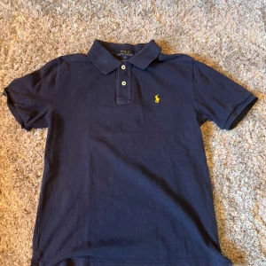 Marinblå pikétröja från Ralph Lauren - Säljer min polo piké då den är storlek  10 till 12 år den har ett litet hål med inte så att man tänker på de här ni frågar elelr funderingar tveka inte på att höra av er 