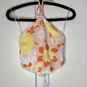 Blommig halterneck linnetopp - HELT NY - Superfin halterneck linnetopp med stora blommor i orange, rosa, gul och vit på ljus bakgrund. Toppen knyts i nacken och har en lätt croppad passform, perfekt för varma dagar och somriga vibes. #haltertopp #Heltny