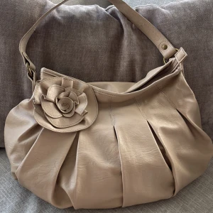 Beige axelväska med rosdetalj - Snygg vintage axelväska i skinn med veckad design och en stor dekorativ ros framtill. 