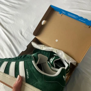 Adidas Campus gröna sneakers 00s - Gröna Adidas Campus sneakers 00s i mocka med vita detaljer och klassiska tre ränder på sidan. Skorna har vit sula, rund tå och snörning. Ingen defekt förutom märket på översta sulan, men inget som försämrar funktionen. Wooow!!😍Dessutom endast använda väldigt få gånger.