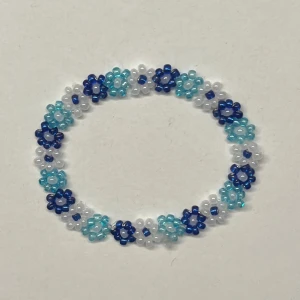 Blommigt pärlarmband i blått och vitt - Superfint armband gjort av små pärlor i blått, vitt och turkost. Pärlorna är formade som små blommor och sitter på en elastisk tråd, vilket gör att storleken kan anpassas. Perfekt accessoar inför sommaren för att ge en färgglad touch💞💞