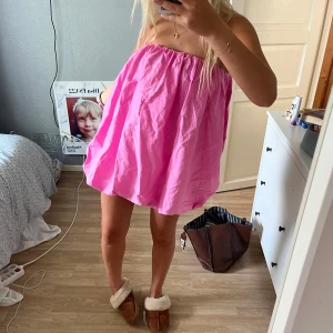 Rosa bubblig kortklänning - Superfin rosa kortklänning med bubblig form och axelbandslös design. Klänningen har en luftig och voluminös siluett, perfekt för dig som vill sticka ut. Materialet känns lätt och somrigt, och färgen är riktigt poppig.
