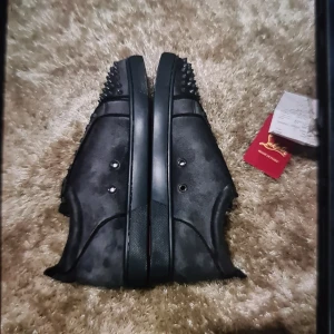 Christian Louboutin svarta sneakers med nitar - Svarta sneakers från Christian Louboutin i mocka med mattsvarta nitar på tån och klassisk röd sula med logga. Skorna har snörning och en stilren, rund tå. Perfekta för dig som vill sticka ut med en edgy vibe.