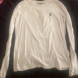 Vit långärmad tröja Polo Ralph Lauren - Vit långärmad tröja från Polo Ralph Lauren i mjuk bomull. Klassisk passform med rund hals och den ikoniska broderade loggan på bröstet. Perfekt basic-plagg som funkar året runt och är lätt att matcha med allt.