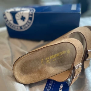 Birkenstock sandaler i beige mocka - OBS!!!! Stora i storleken rekommenderar att testa i affär först👍👍Snygga Birkenstock sandaler i beige mocka med två breda remmar och justerbara metallspännen. Fotbädden är anatomiskt utformad för extra komfort och sulan är svart. Perfekta för chill dagar och sommarhäng. Helt nya, alla taggar ovh box ingår.