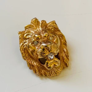 Guldig lejonhuvud med strassdetaljer - Unik sjalclip i form av ett lejonhuvud i guldtonad metall med glittrande strass i ögonen och munnen. Ringen har en cool, tredimensionell design som verkligen sticker ut och ger ett lyxigt statement till din stil. Vintage. West Germany 