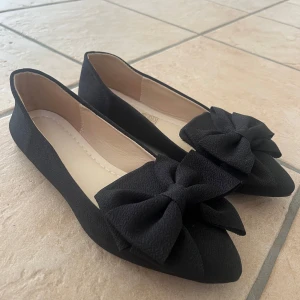 Svarta ballerinaskor med rosett - Stilrena svarta ballerinaskor med spetsig tå och rosetter fram. Storlek 38