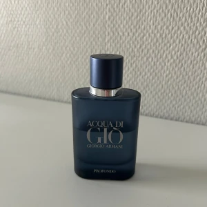 Acqua di Giò Profondo parfym - Acqua di Giò ProfondO EdP från Giorgio Armani är en elegant herrparfym i en stilren, mörkblå glasflaska med silverdetaljer och matchande blått lock. Parfymen innehåller bland annat noter av citrus och marin, vilket gör den till en perfekt sommarparfym. Flaskan är 40ml, men som ses i bilden är lite över hälften kvar.